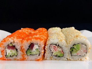 Sushi with red fish and avocado, close-up, on a black background. Japanese traditional cuisine, delicious sushi with dill and sesame seeds. Rolls - California and Philadelphia.