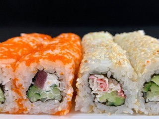 Sushi with red fish and avocado, close-up, on a black background. Japanese traditional cuisine, delicious sushi with dill and sesame seeds. Rolls - California and Philadelphia.