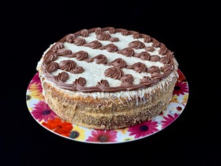 Round cake with cream patterns, on a black background. A sweet birthday present for a teenager. A festive dessert for the whole family. Baking with icing on a plate.