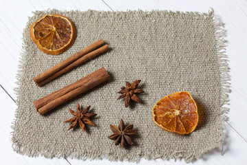 Anise, cinnamon sticks and slices of dried tangerines. Lying on a piece of linen. Against the background of white painted boards.