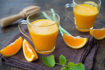 Two glass mugs of freshly squeezed orange juice stand on a wooden background. Horizontal orientation.