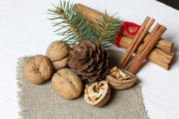 Walnuts, cinnamon sticks and spruce branch with pine cone. Lying on a piece of linen. Against the background of white painted boards.