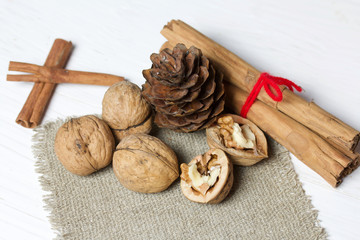 Walnuts, cinnamon sticks and fir cone. Lying on a piece of linen. Against the background of white painted boards.