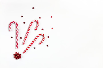 Christmas composition three caramel candy canes, confetti stars and red bow on white background with copy space. Festive minimal style flat lay. For greeting card, invitation. Horizontal