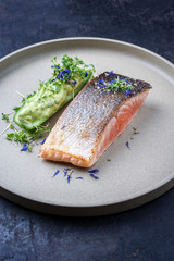Minimalistic design salmon fish filet glazed with avocado and wasabi creme in a sliced cucumber as closeup on a modern design plate decorated with herbs
