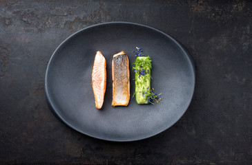Minimalistic design salmon fish filet glazed with avocado and wasabi creme in a sliced cucumber as...