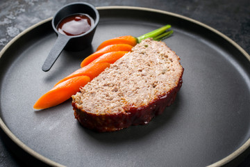 Minimalistic gourmet meatloaf slice with sliced carrot and ketchup as closeup on a modern design plate with copy space