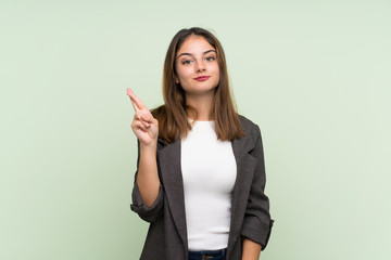 Obraz premium Young brunette girl with blazer over isolated green background with fingers crossing and wishing the best