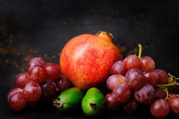 Different fruits and berries on black background, vitamin concept. Pomegranate, grapes and feijoa.