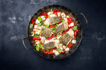 Traditional fried Greek cod fish filet casserole with feta cheese and vegetable as top view in a...