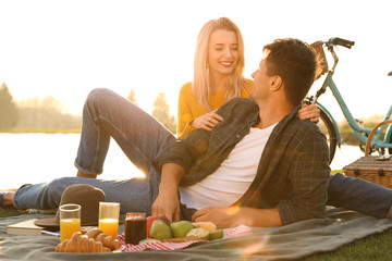 Happy young couple having picnic near lake on sunny day