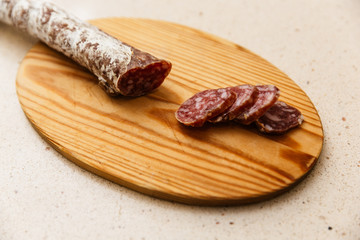 un fuet  espetec (longaniza catalana) cortado a cuchillo encima de tabla de madera a cuchillo. encima de mármol claro de cocina 