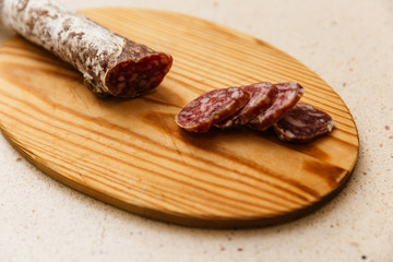 un fuet  espetec (longaniza catalana) cortado a cuchillo encima de tabla de madera a cuchillo. encima de mármol claro de cocina 