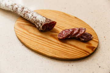 un fuet  espetec (longaniza catalana) cortado a cuchillo encima de tabla de madera a cuchillo. encima de mármol claro de cocina 