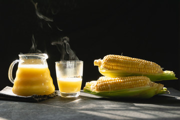 The steam from a jug and a glass of corn milk on black background, Warm drinks make good...