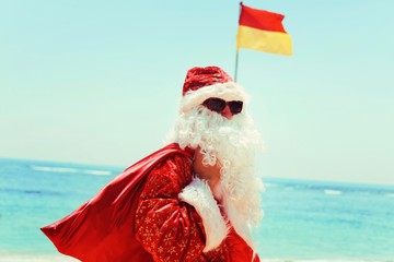 Santa Claus with a red bag of gifts near the Pacific ocean on a tropical island resting against the...
