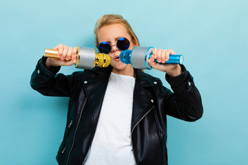 stylish european girl in sunglasses singing in two microphones on a light blue background