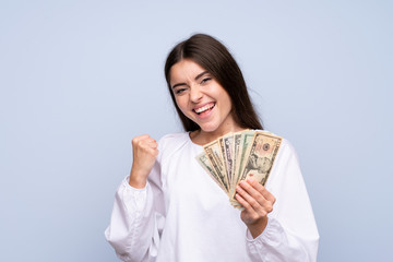 Young woman over isolated blue background taking a lot of money