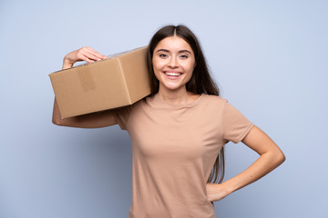 Young woman over isolated blue background holding a box to move it to another site