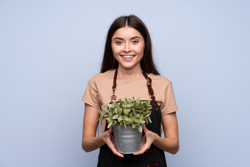 Young woman over isolated blue background taking a flowerpot