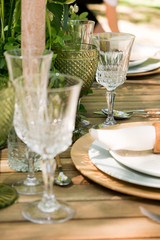 Festive table decor in openair next to the pond. Green color with wooden cutlery. Different natural white flowers. Wooden table and chairs. Wine glasses. Luxury wedding, party, birthday.