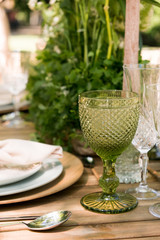 Festive table decor in openair next to the pond. Green color with wooden cutlery. Different natural white flowers. Wooden table and chairs. Wine glasses. Luxury wedding, party, birthday.