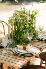Festive table decor in openair next to the pond. Green color with wooden cutlery. Different natural white flowers. Wooden table and chairs. Wine glasses. Luxury wedding, party, birthday.