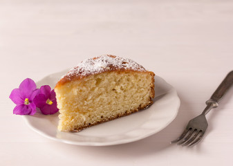 piece of homemade lemon pie on a white plate with violet flowers and on a white background