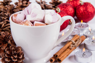 Cup of hot chocolate with marshmallows ,  some cinnamon sticks, cones, christmas balls and candles