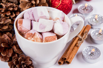 Cup of hot chocolate with marshmallows ,  some cinnamon sticks, cones, christmas balls and candles