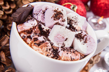 Cup of hot chocolate with marshmallows, and some cinnamon sticks, cones, christmas balls and candles