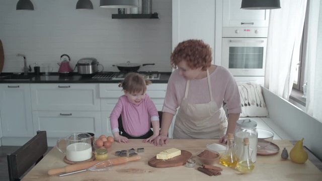 A girl learns to cook cookies in the kitchen with her mother.
