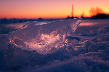 A piece of clear ice close up on snow at sunset