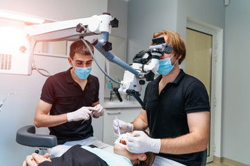 Male dentist with dental tools - microscope, mirror and probe treating patient teeth at dental clinic office. Medicine, dentistry and health care concept. Dental equipment