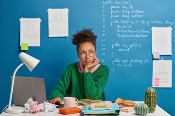 Ethnicity woman poses at worktable, looks away, being distracted from work, ponders about something...
