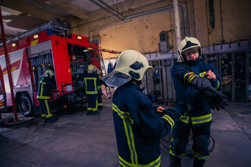 Firefighters preparing their uniform and the firetruck in the background inside the fire station