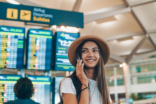 girl in a continental hat listens to the phone on the background of the airport scoreboard and smiles