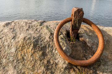 Rusty ring for the mooring of a boat on the rock by the ocean