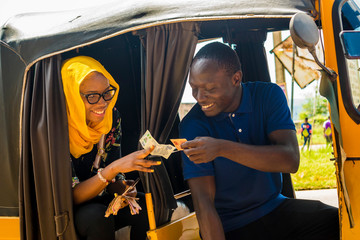 young african woman sitting in the back seat of an auto rickshaw taxi paying the driver