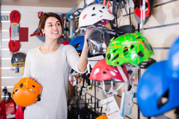 cheerful female shopper examining helmets in sports equipment store