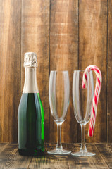 Bottle with sparkling wine and red caramel in glassware. Wooden background. Christmas and New Year celebration.