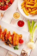 Barbecued chicken wings with french fries and vegetable salad on timber