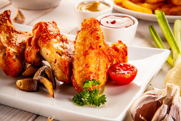 Barbecued chicken wings with french fries and vegetable salad on timber