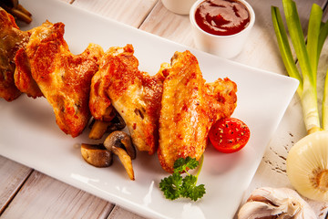 Barbecued chicken wings with french fries and vegetable salad on timber