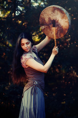 beautiful shamanic girl playing on shaman frame drum in the nature.
