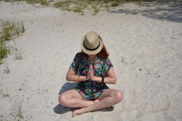 Fototapeta na wymiar girl on the beach red-haired girl girl in a hat yoga meditation 