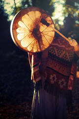 beautiful shamanic girl playing on shaman frame drum in the nature.