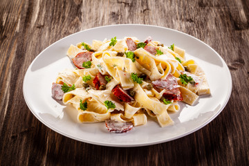 Pasta with cream sauce and sausages on wooden background