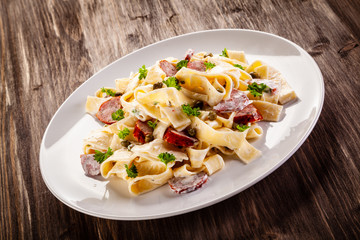 Pasta with cream sauce and sausages on wooden background