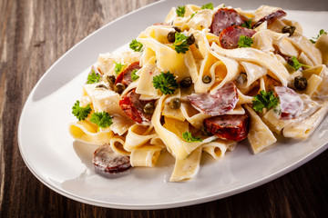 Pasta with cream sauce and sausages on wooden background